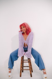 a woman with pink hair sitting on a stool
